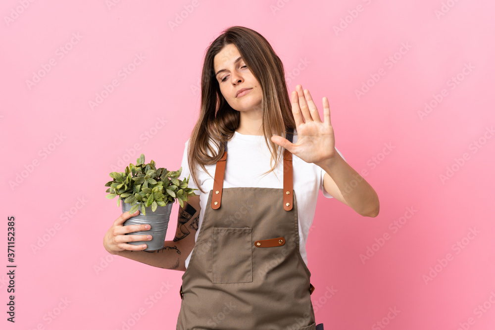 Gardener woman holding a plant isolated on pink background making stop gesture and disappointed Gardener woman holding a plant isolated on pink background making stop gesture and disappointed