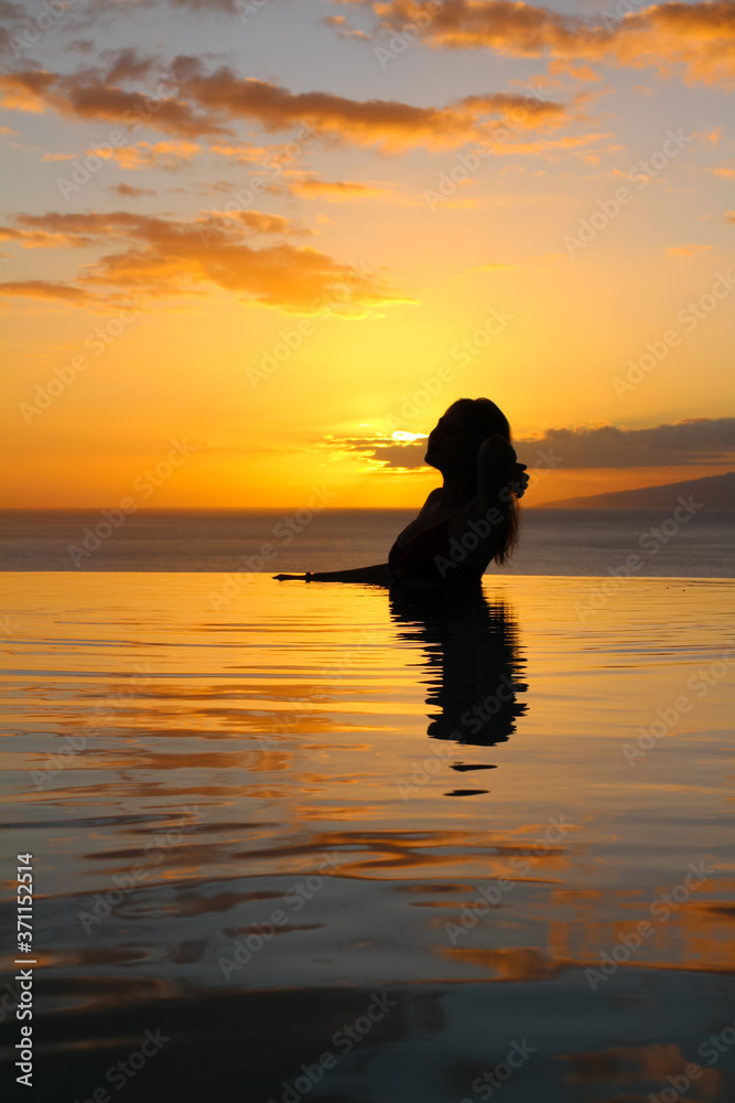 the Girl is bent over in the pool, her hand supporting her loose hair, against the background of a beautiful sunset. hotel Las Terrazas de Abama