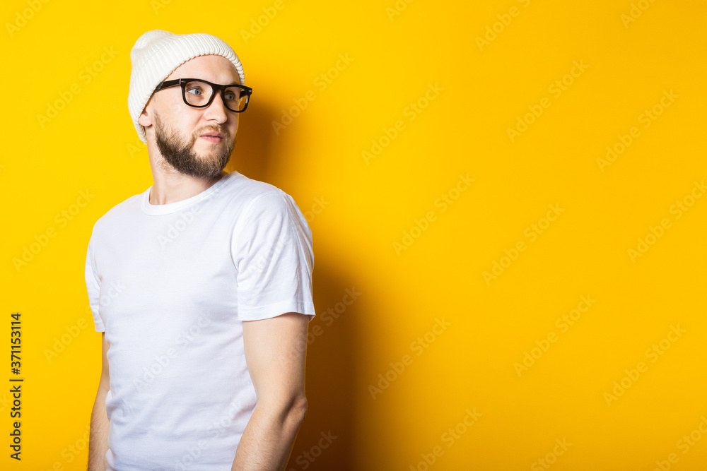 Bearded young guy in a cap, in a white T-shirt and glasses on a yellow background. Bearded young guy in a cap, in a white T-shirt and glasses on a yellow background.