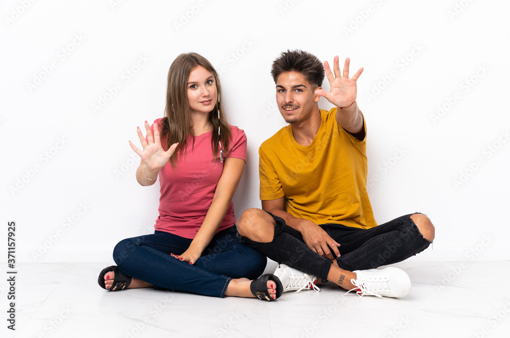 Young couple sitting on the floor isolated on white background counting five with fingers Young couple sitting on the floor isolated on white background counting five with fingers