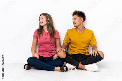 Young couple sitting on the floor isolated on white background laughing in lateral position