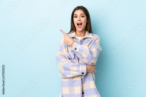 Young caucasian woman isolated on blue background surprised and pointing side