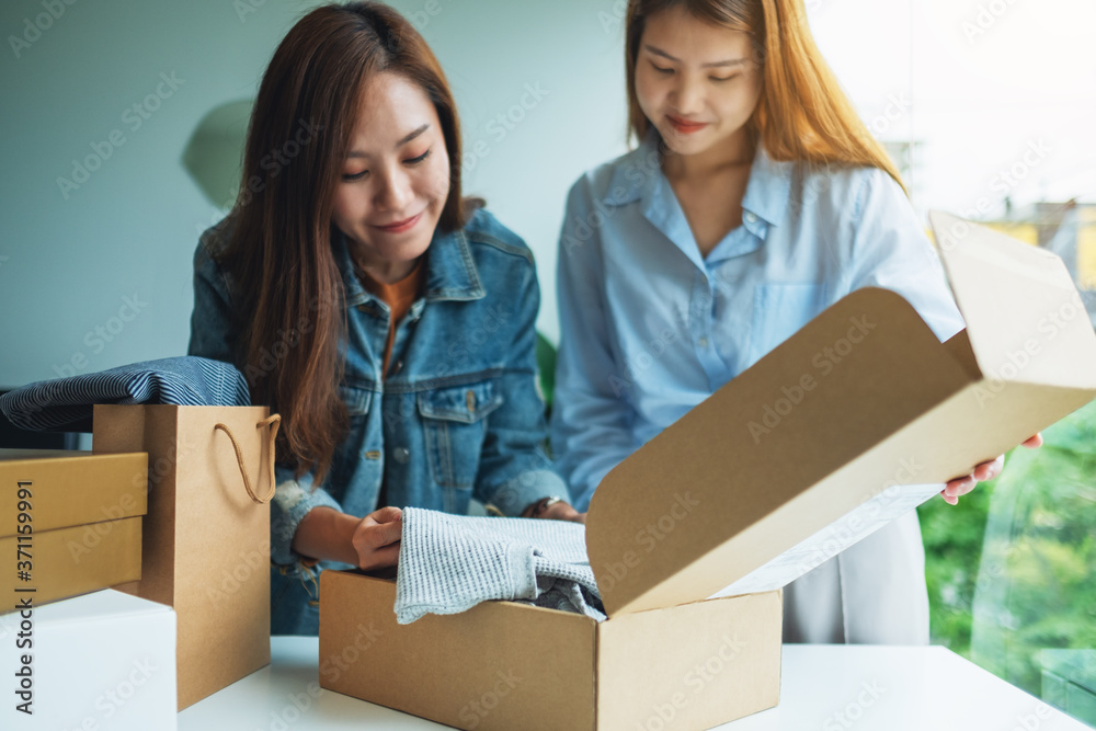 Two young women receiving and opening a postal parcel box of clothing at home for delivery and online shopping concept Two young women receiving and opening a postal parcel box of clothing at home for delivery and online shopping concept