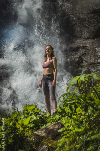 young woman standing in front of a beautiful wild waterfall in a mountain forest Austria