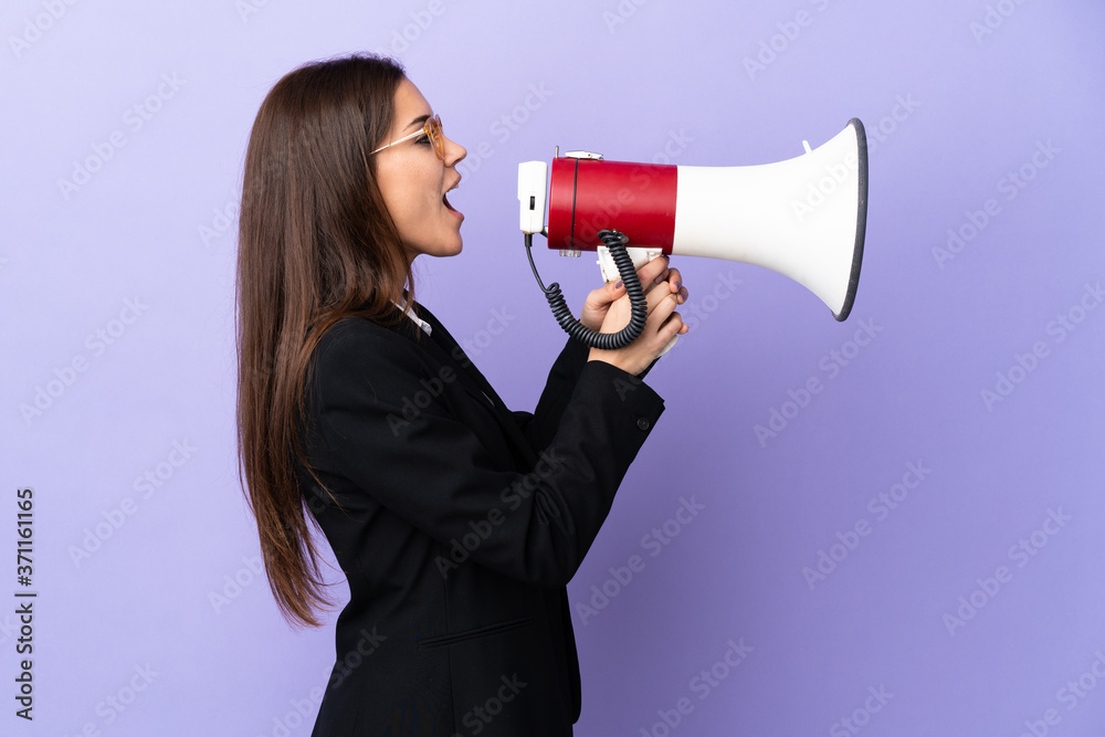 Business woman isolated on purple background shouting through a megaphone
