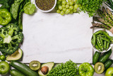 Green vegetables and fruits, greens and legumes and a white marble board on a white background. Healthy food and clean eating concept.