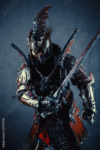 Powerful knight in the armor with the sword. Dark background.