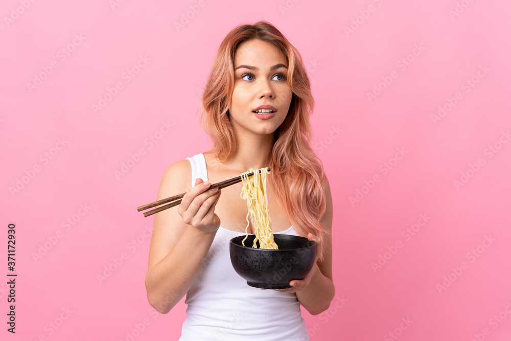 Teenager girl over isolated pink background holding a bowl of noodles with chopsticks and looking up Teenager girl over isolated pink background holding a bowl of noodles with chopsticks and looking up