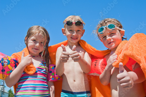 drei Kinder in Badesachen mit orangem Badetuch