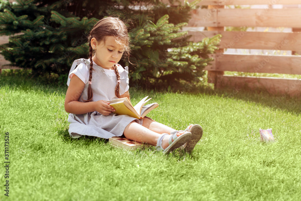 Cute schoolgirl with pigtails laying on grass while reading book. Cute schoolgirl with pigtails laying on grass while reading book.
