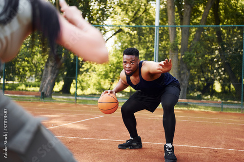 Fototapeta Naklejka Na Ścianę i Meble -  African american man with girl plays basketball on the court outdoors