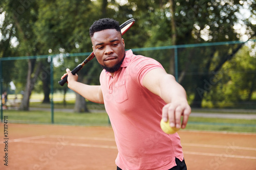 African american man in pink shirt plays tennis on the court outdoors