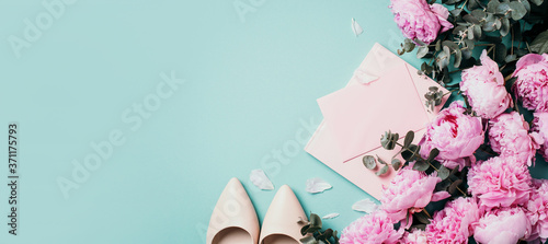 Fashion feminine blogger concept. Feminine workspace with notebook, shoes, pink peony, eucalyptus flower on blue background. Top view, copy space. Blogger, feminine business concept. Flat lay. © jchizhe