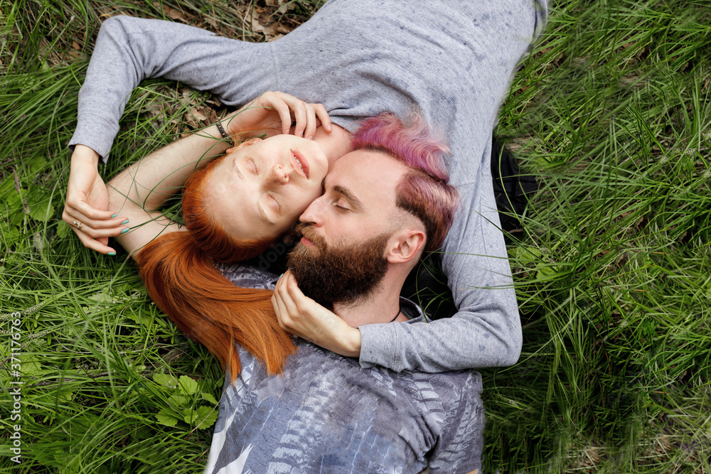 Top view of a hipster couple, seated down on a green grass, seated down with turned heads with closed eyes. Couple relationship. Top view of a hipster couple, seated down on a green grass, seated down with turned heads with closed eyes. Couple relationship.