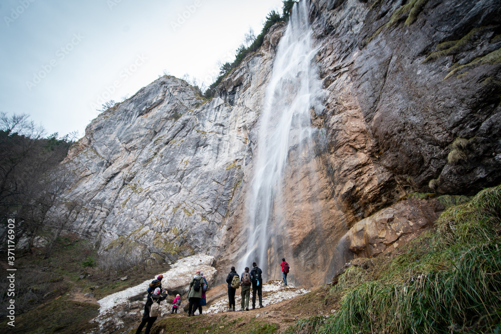 Experienced hiker standing in front of a waterfall with his teammates Experienced hiker standing in front of a waterfall with his teammates