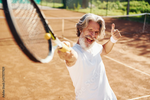 Playing game. Senior modern stylish man with racket outdoors on tennis court at daytime © standret