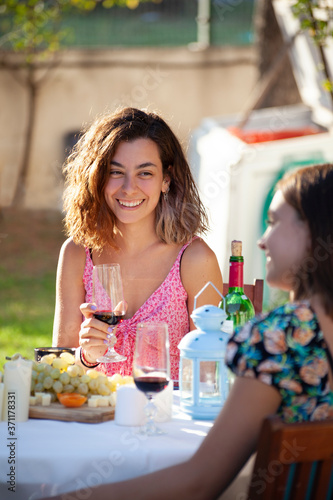 Young beautiful woman enjoying wine at backyard sitting with her friend