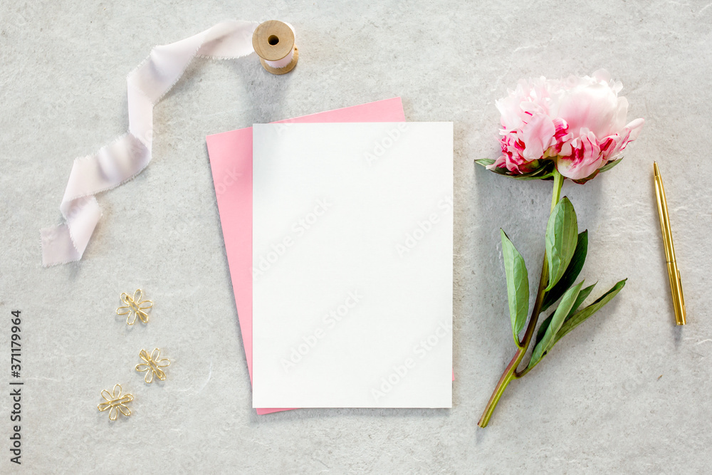Mockup invitation, blank paper greeting card, pink envelope and peonies on gray stone table. Flower background. Flat lay, top view. Mockup invitation, blank paper greeting card, pink envelope and peonies on gray stone table. Flower background. Flat lay, top view.