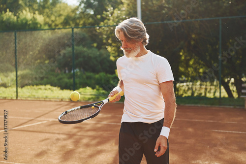 Training time. Senior modern stylish man with racket outdoors on tennis court at daytime