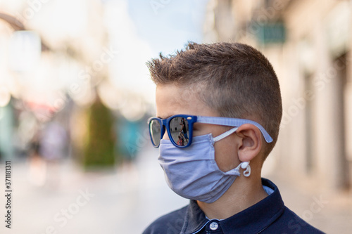 Close-up of a kid with medical mask and sunglasses in the street. Coronavirus pandemic concept