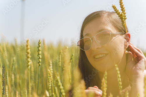 Close-up of a smiling white woman's face in a field among the ears of wheat. Summer, autumn, harvest, hippies, unity with nature.