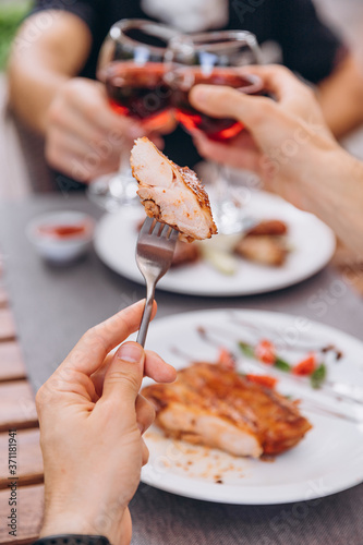 piece of fried meat (steak or kebab) on a fork on the background of a table in a restaurant on a summer playground in the company of friends, focus on a dish with a blurred background