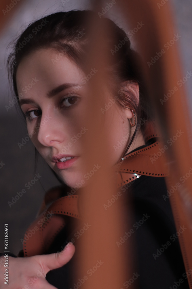 brunette girl in a black turtleneck wrapped in a film reel on a gray wall background brunette girl in a black turtleneck wrapped in a film reel on a gray wall background