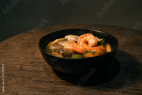 Thai Spicy Mixed Vegetable Soup with Prawns (Gang Liang) on black black bowl wooden table isolated on Dark Slate Gray Concrete Wall background photo