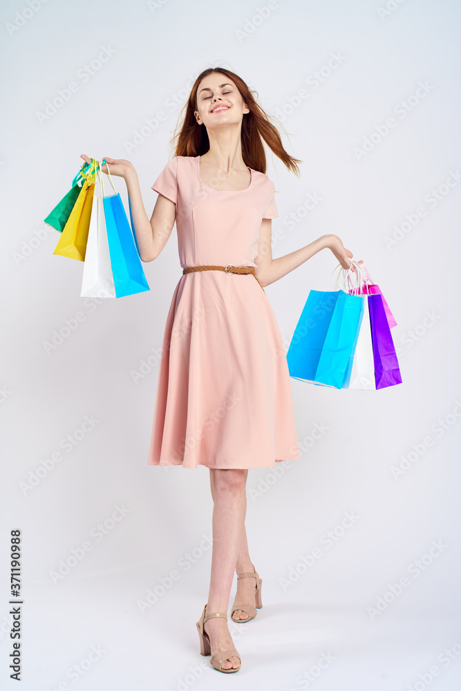 nice girl in a pink dress with shopping bags in her hands in full growth on a light background indoors