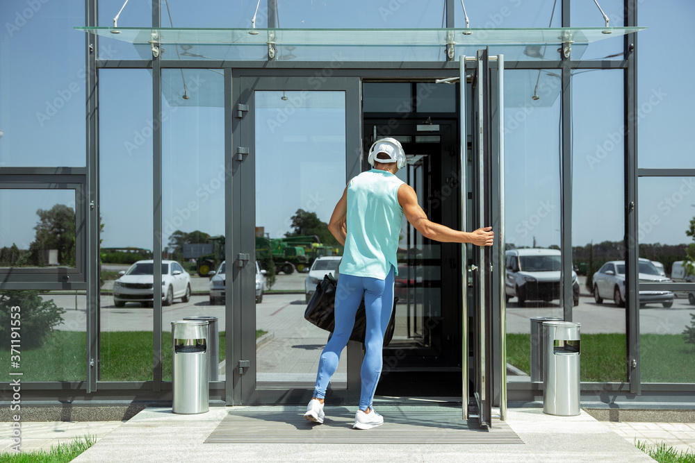 On the way. Sportsman walking down against modern glassed building, airport in megapolis. Before flight to competition. Professional stylish, confident athlete. Journey, vacation, sport lifestyle.