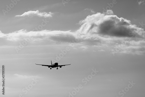 an airplane flying in the sky with cloud in monochrome