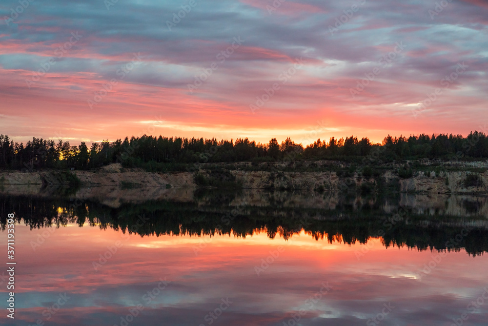 Colorful sunset with a mirror reflection in a forest lake .