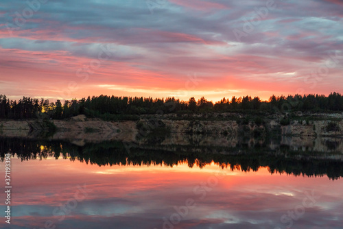 Colorful sunset with a mirror reflection in a forest lake .