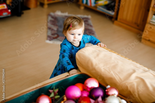 Cute baby girl taking down holiday decorations from Christmas tree. child holding light garland. Family after celebration remove and dispose tree