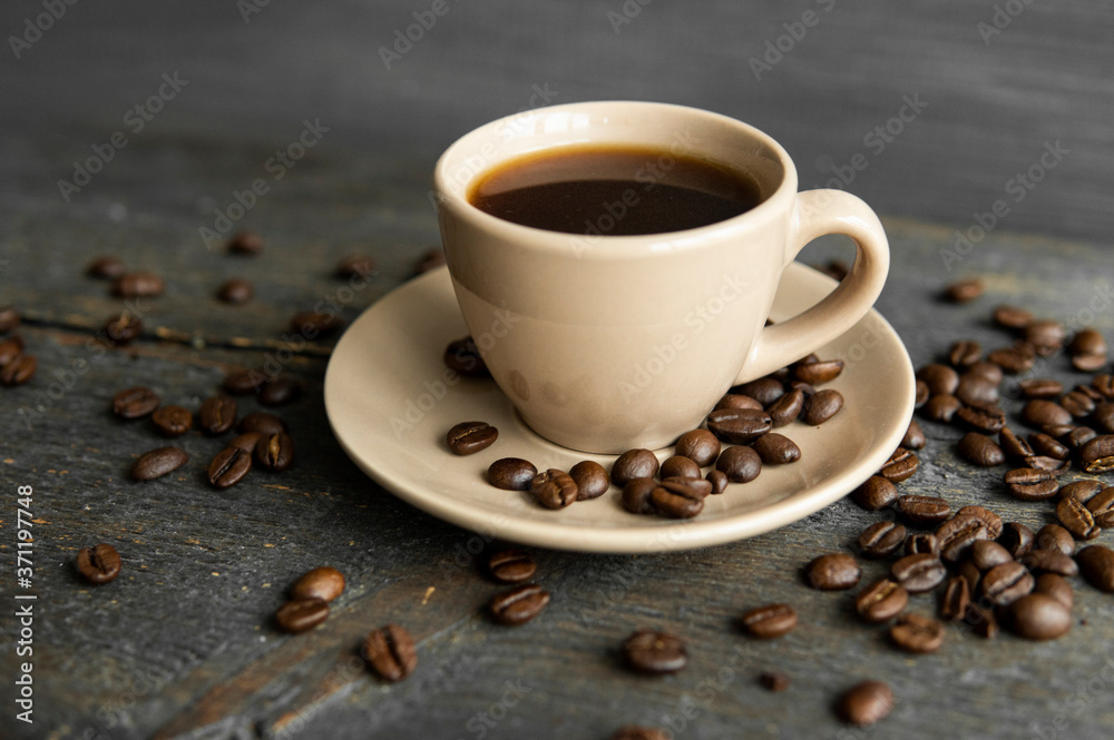 Coffee cup with roasted coffee beans on wooden table background. Mug of black coffe with scattered coffee beans on a wooden table. Fresh coffee beans.