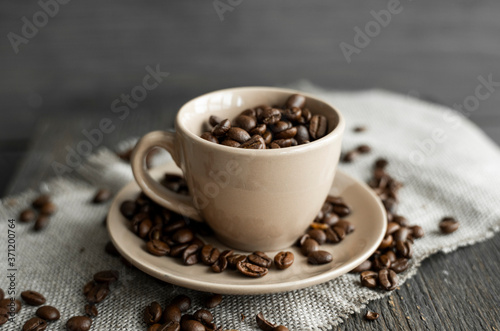 Coffee cup filled of fresh arabica or robusta coffee beans with scattered coffee beans on a linen textile and wood table.