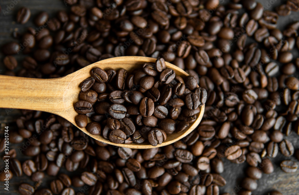 Fresh roasted arabica coffee beans in a wooden spoon and scattered coffee beans on a wooden table.