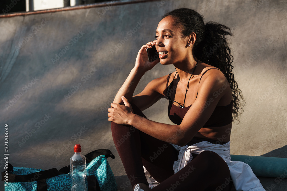 Obraz premium Photo of smiling african american sportswoman talking on mobile phone