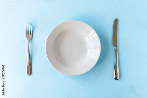 empty plate, knife and fork on light blue background