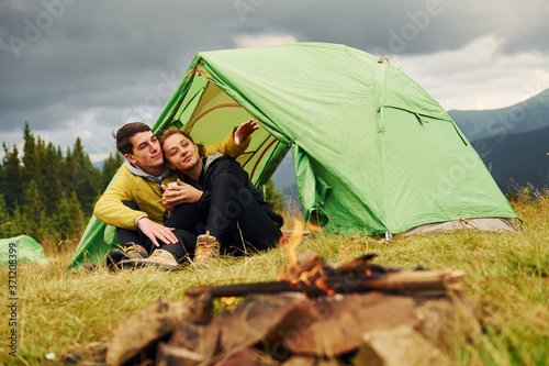 Guy with his girlfriend sits near tent. Majestic Carpathian Mountains. Beautiful landscape of untouched nature