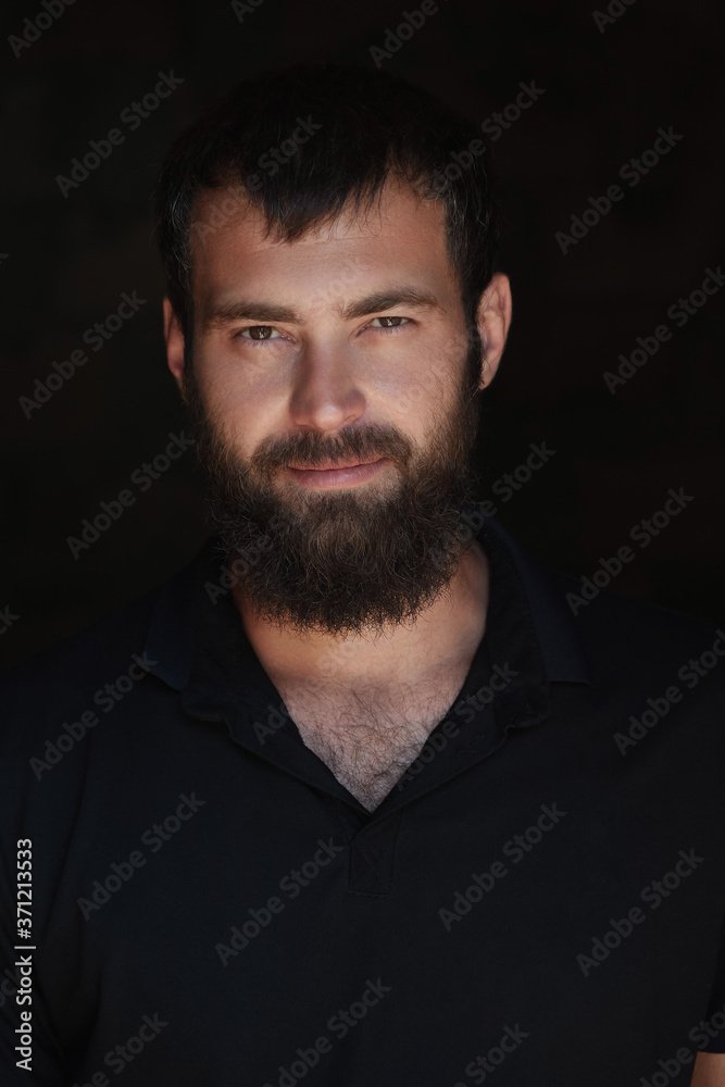 Man showing severe emotion. Beardy male in black t-shirt on dark background with serious look.