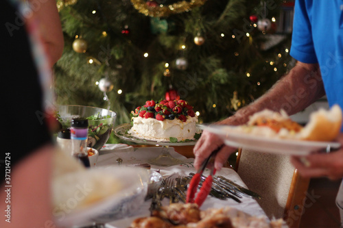 Pavlova with cream & berries – Australian dessert. Christmas family buffet lunch with Christmas tree with lights and baubles.