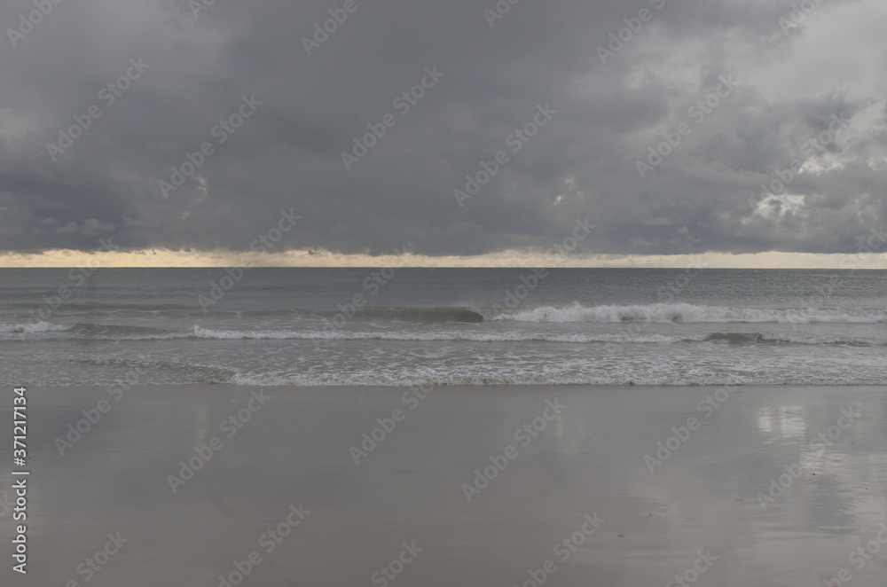 Colorful stormy beach sky, wide array of yellow, muted gray,purple, blue, pink and white, sand, unique seascape  or landscape, with reflection on the beach and pacific ocean with waves, drama, weather
