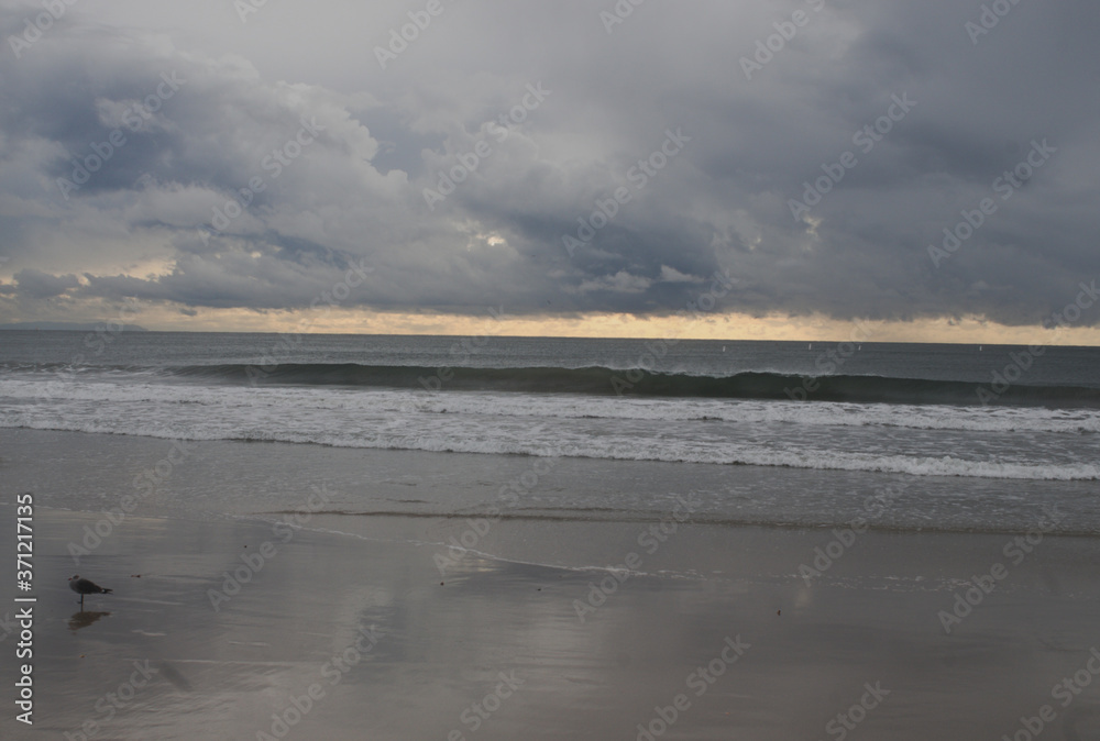 Colorful stormy beach sky, wide array of yellow, muted gray,purple, blue, pink and white, sand, unique seascape  or landscape, with reflection on the beach and pacific ocean with waves, drama, weather