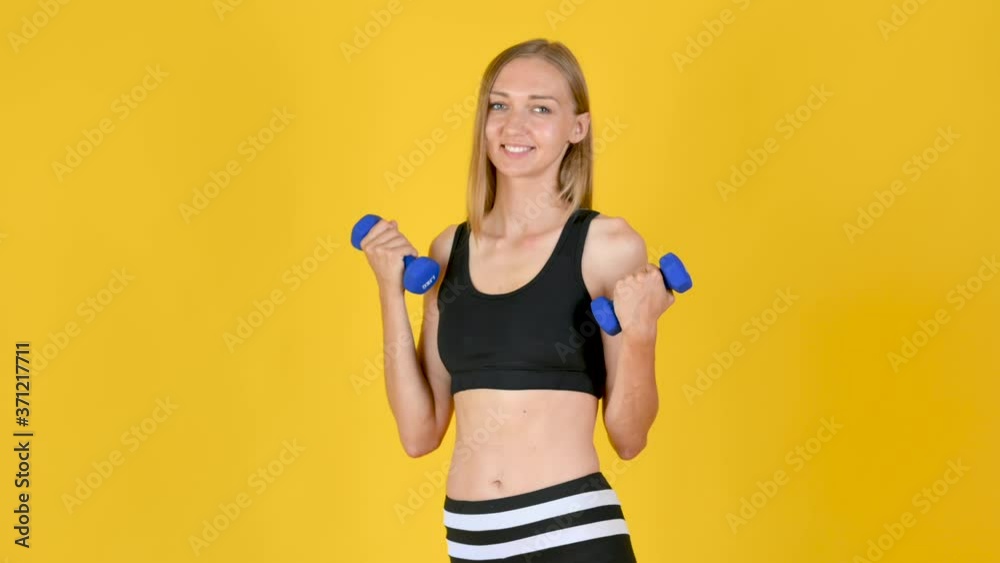 Portrait of an attractive young girl in sportswear doing exercises with dumbbells. Isolated on a yellow background Portrait of an attractive young girl in sportswear doing exercises with dumbbells. Isolated on a yellow background