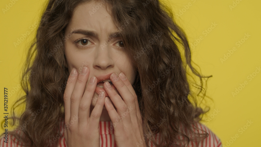 Afraid woman face with open mouth touching face with hands on yellow background Afraid woman face with open mouth touching face with hands on yellow background