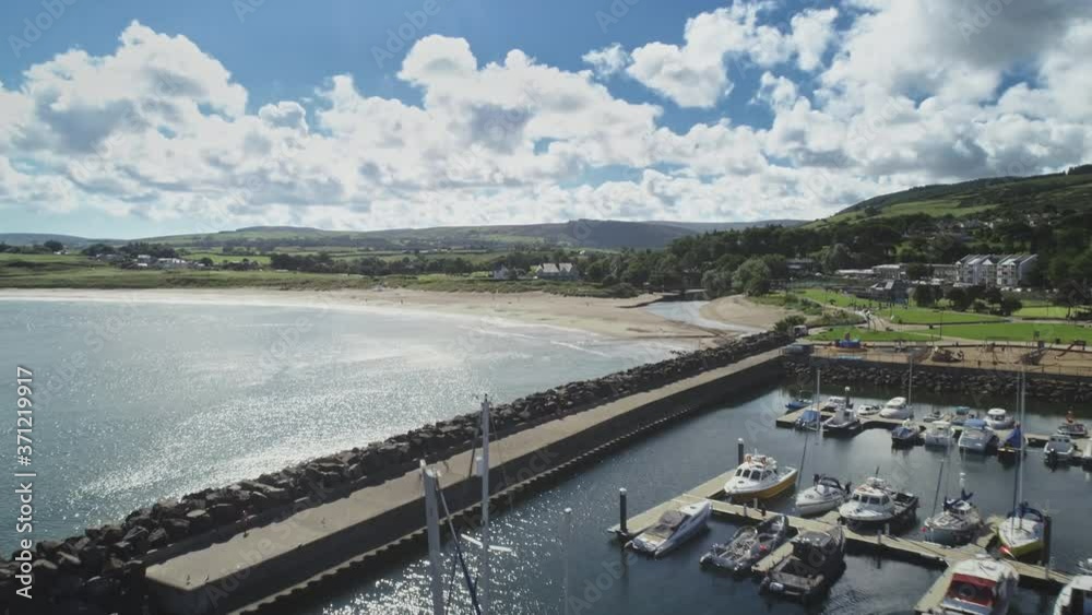 Ireland yachts, gulf harbor aerial view over Atlantic ocean coast. Wide fields, green meadows, sandy beach, hills villages under cloudy sky. Epic rural scape of Ballycastle pier. Shot in 4K, UHD