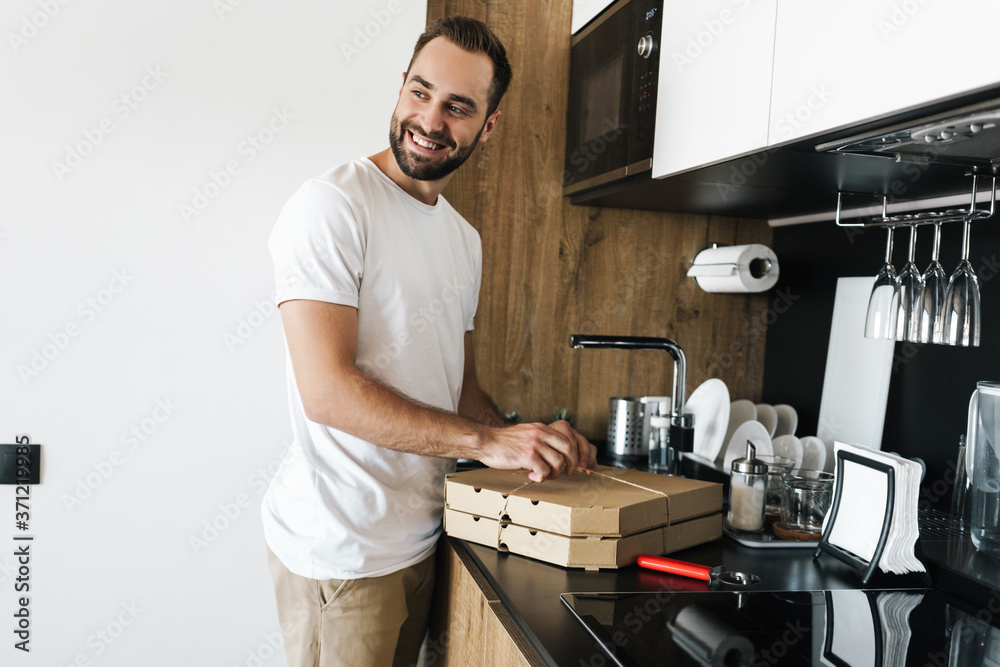 Image of young happy guy smiling and opening boxes with pizza