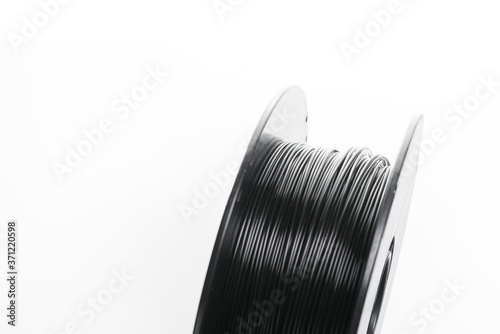 A spool of black 3d printer filament, up close. Black PLA filament wound up on a spool, ready to be made into an item or part with additive manufacturing.