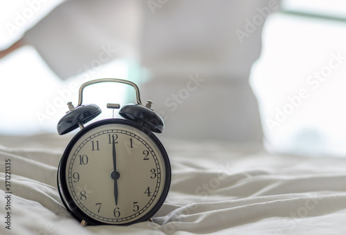 Woman on bed wake up stretching in bedroom with alarm clock at 6.00 a.m. morning. Biological Clock healthcare concept